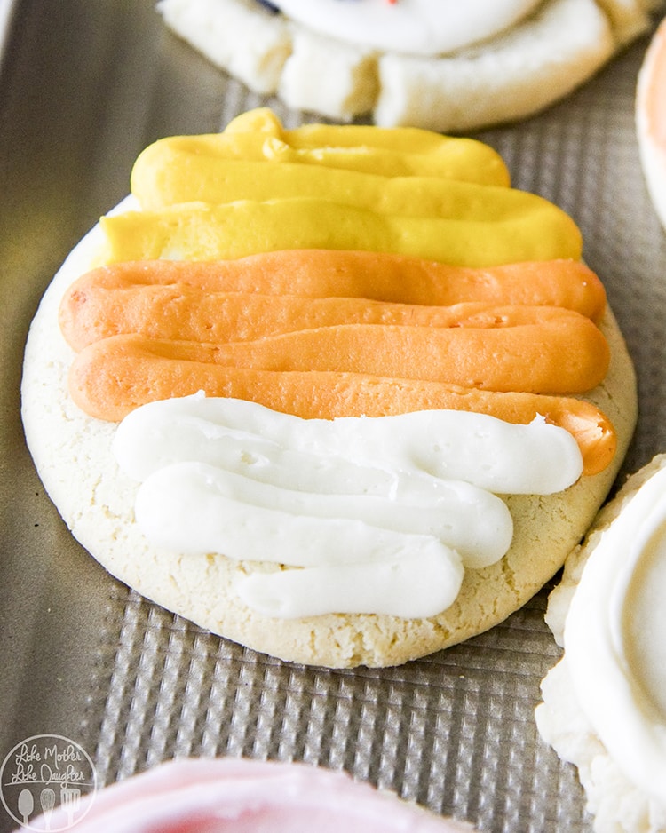 A round sugar cookie decorated with white, orange, and yellow frosting, like candy corn.