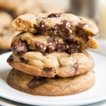 Close up image of stacked brown butter chocolate chunk cookies on a white plate with oozing chocolate.