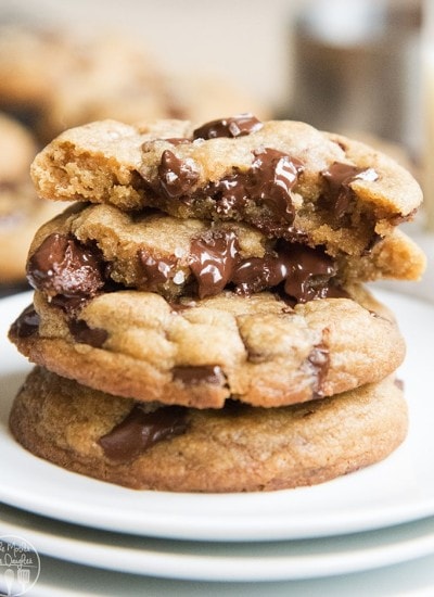 Close up image of stacked brown butter chocolate chunk cookies on a white plate with oozing chocolate.