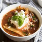 A bowl of lasagna soup topped with ricotta and fresh basil.