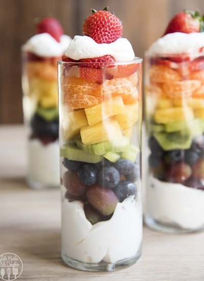 A parfait in a glass with a layer of whipped cream, and a rainbow assortment of colorful fruit.