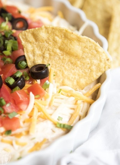 Taco dip topped with shredded cheese, and diced tomatoes in a platter.