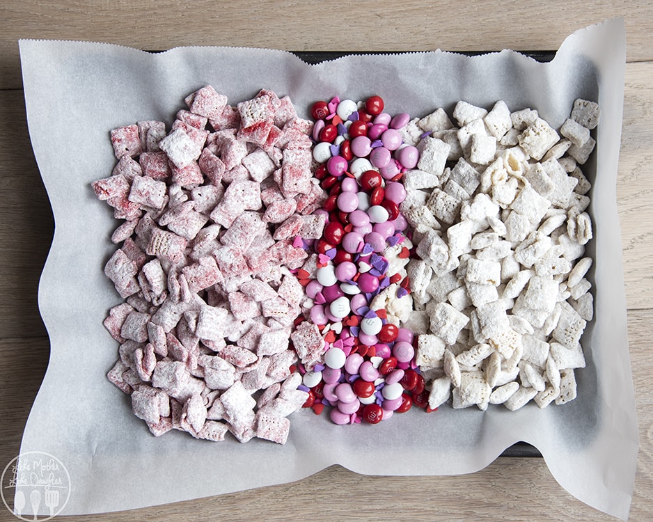 A tray of pink puppy chow, valentine m&ms, and white puppy chow. 