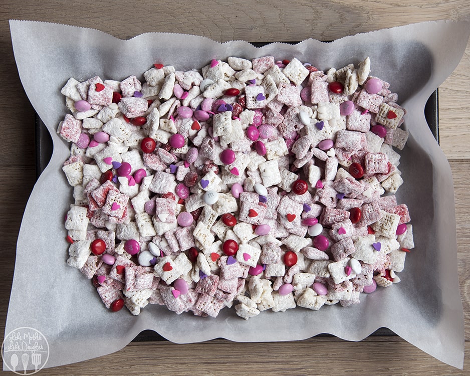 A baking tray topped with a strawberry puppy chow full of red and pink m&ms. 