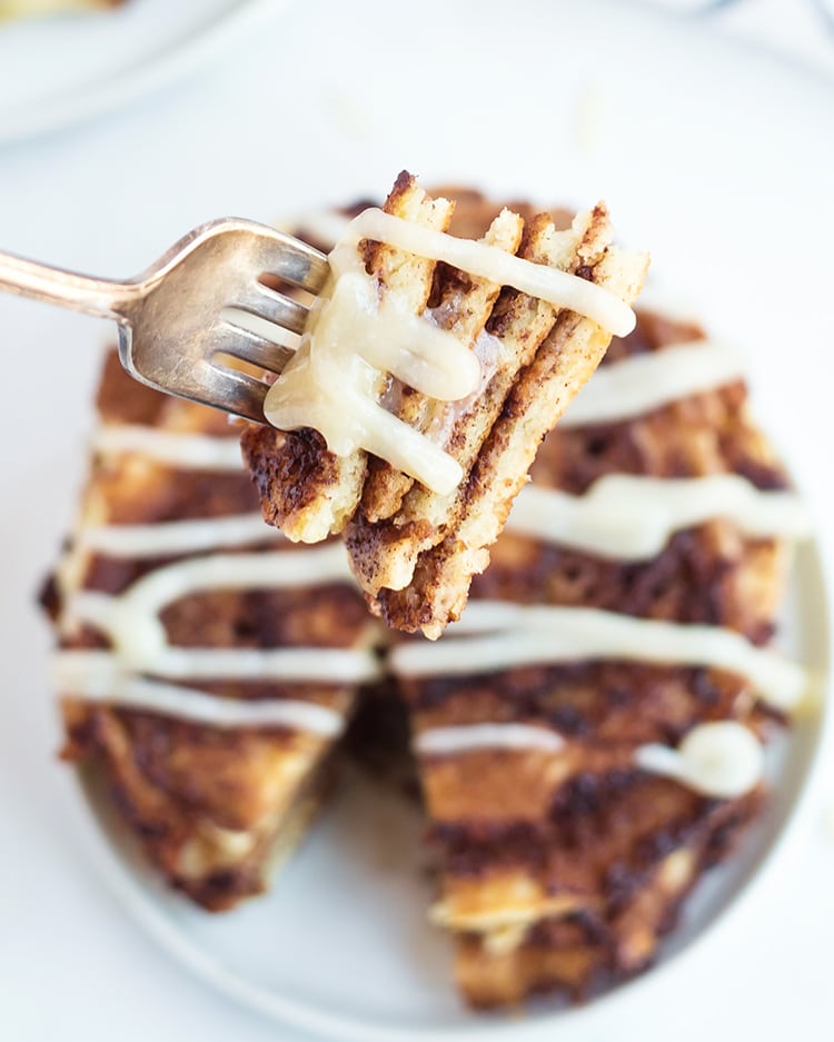 A bite of cinnamon roll pancakes on a fork with cream cheese frosting over the top