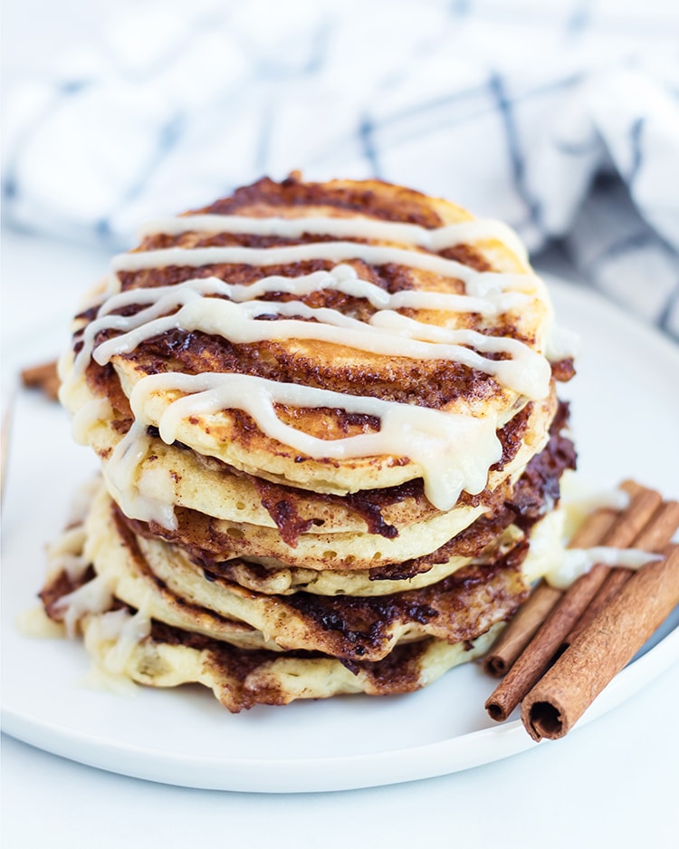A stack of cinnamon roll pancakes drizzled with cream cheese frosting on a plate