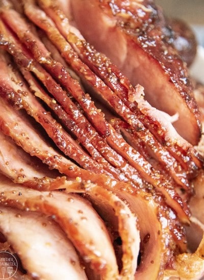 A close up of a sliced ham covered in a sticky looking sauce, you can see mustard seeds in the sauce.