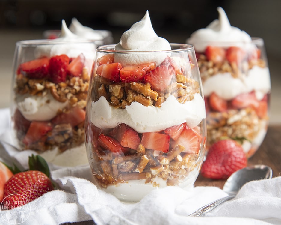 Strawberry pretzel parfaits in glasses with no bake cheesecake, sweetened pretzels, and chopped up strawberries, each layered.