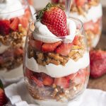 A parfait of whipped cream, chopped up pretzels, strawberries, and a fresh strawberry on top.
