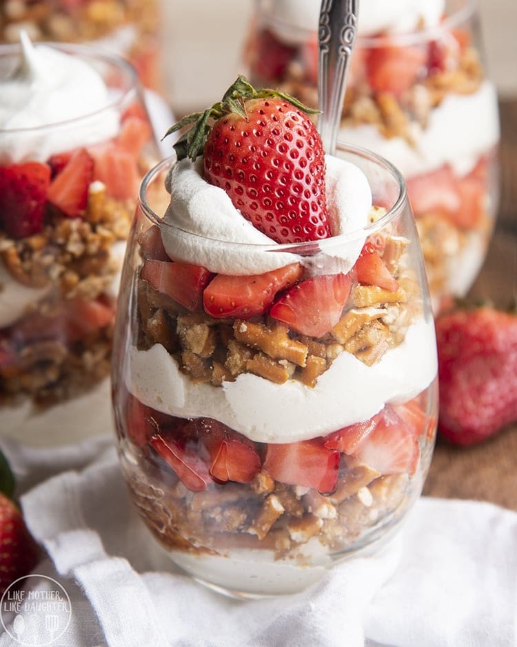A parfait of whipped cream, chopped up pretzels, strawberries, and a fresh strawberry on top.