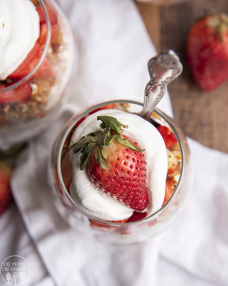 An overhead of a strawberry pretzel parfait in a glass, with a fresh strawberry on top.