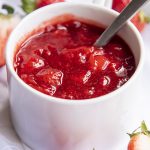 Close up image of a strawberry sauce in a white bowl with a spoon.