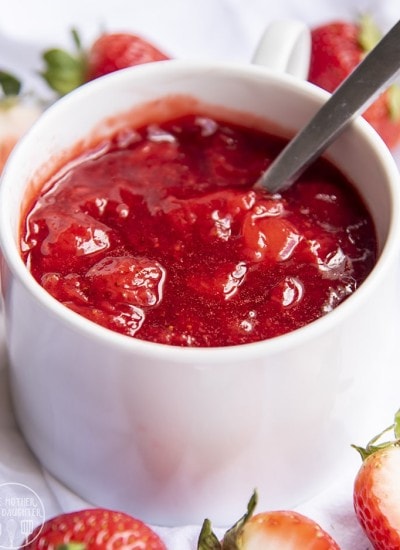 Close up image of a strawberry sauce in a white bowl with a spoon.