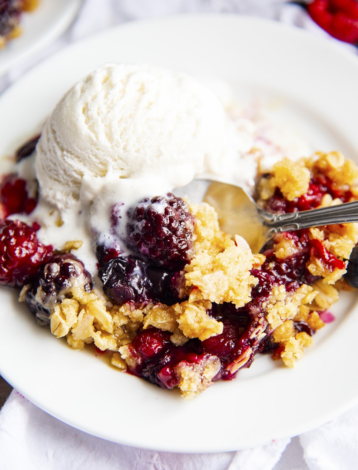 A plate of berry crisp with ice cream on top, and a spoon in it.
