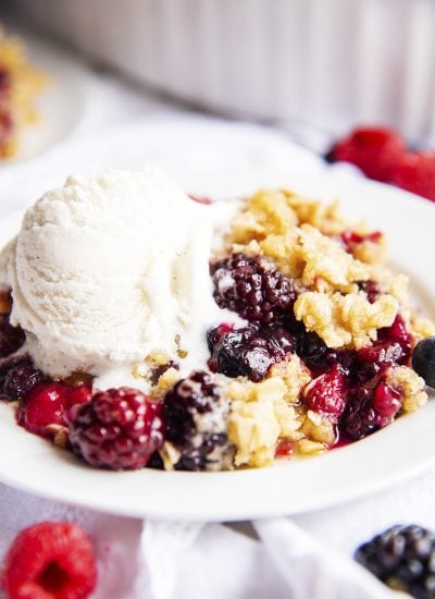 A white plate topped with berry crisp and ice cream melting on to it.