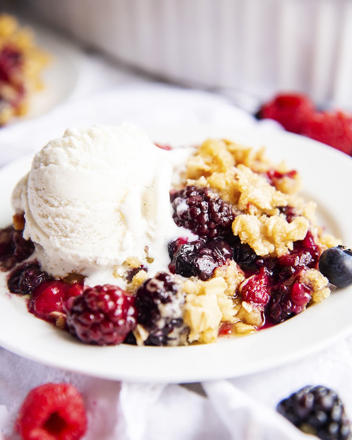 A white plate topped with berry crisp and ice cream melting on to it.