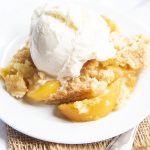 A peach cobbler dump cake with a scoop of vanilla ice cream on top.