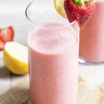 A glass of strawberry lemonade smoothie with a strawberry and lemon wedge on top.