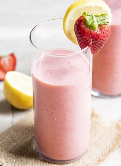 A glass of strawberry lemonade smoothie with a strawberry and lemon wedge on top.