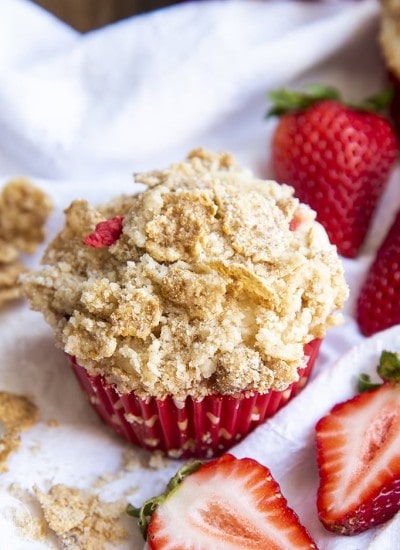 Close up shot of strawberry yogurt muffins with crumble on top and strawberries in background.