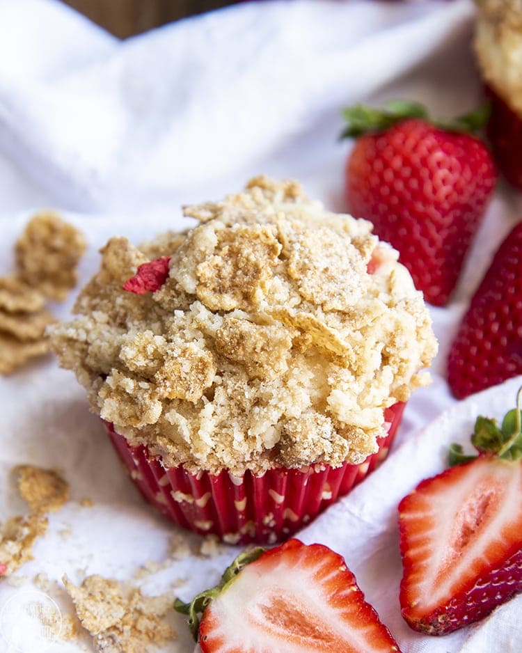 Close up shot of strawberry yogurt muffins with crumble on top and strawberries in background.
