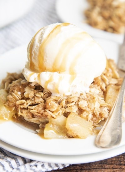 A plate of apple crisp with an oatmeal topping and a scoop of vanilla ice cream on top.