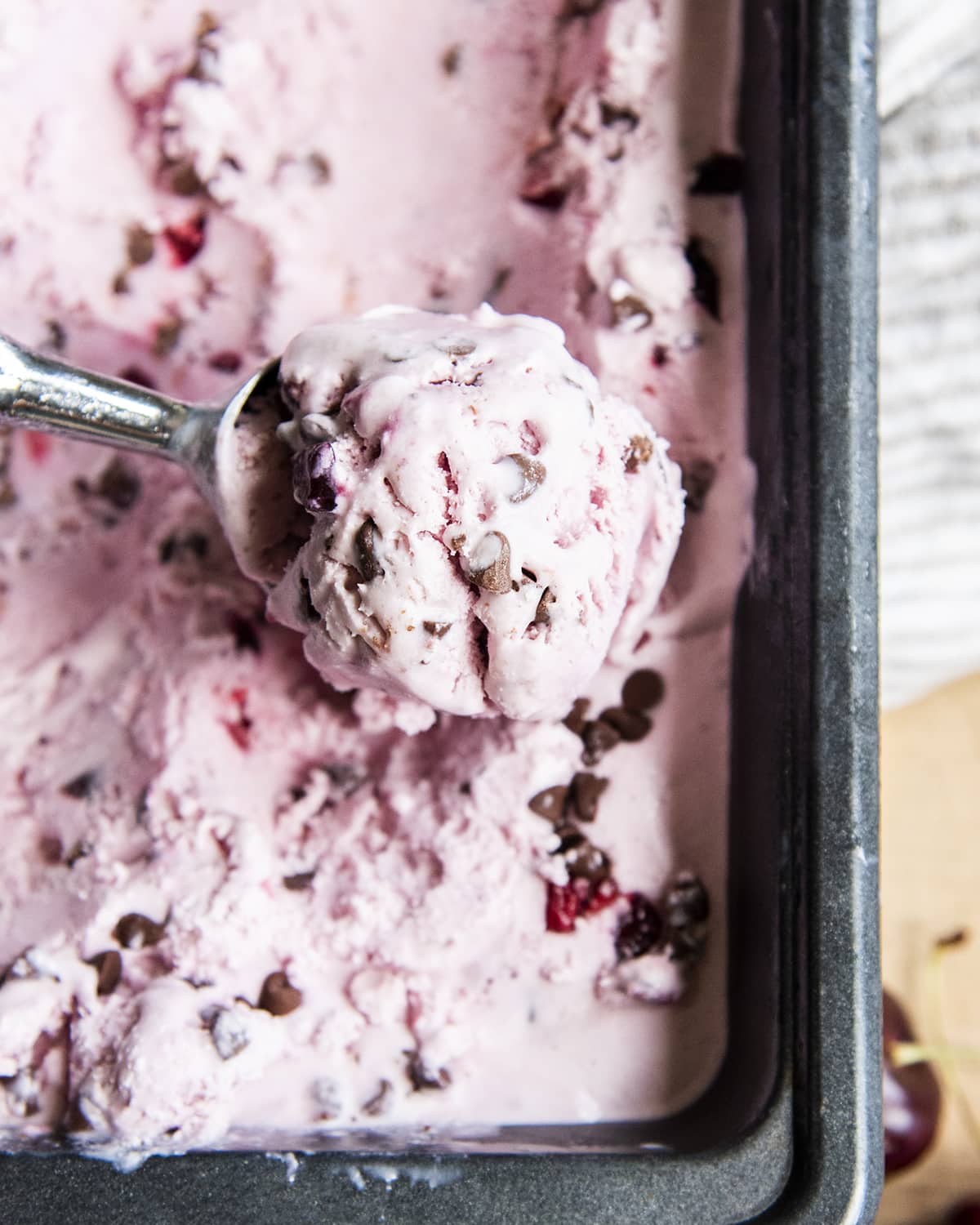 A scoop of cherry chocolate chip ice cream above a container of it.