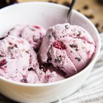 A bowl of scoops of cherry ice cream with chocolate chips in it.
