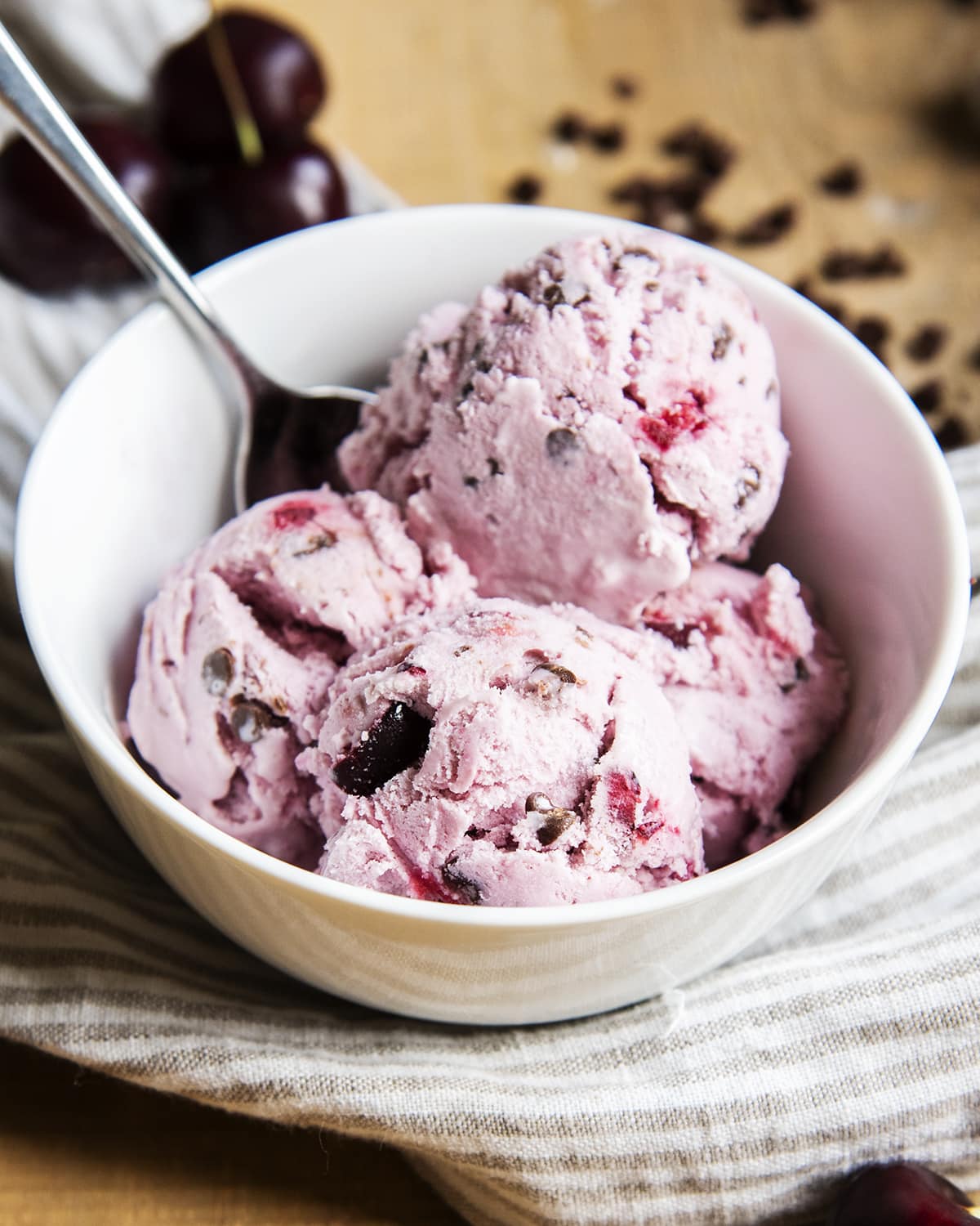 A bowl of pink cherry ice cream with cherry chunks and chocolate chips.