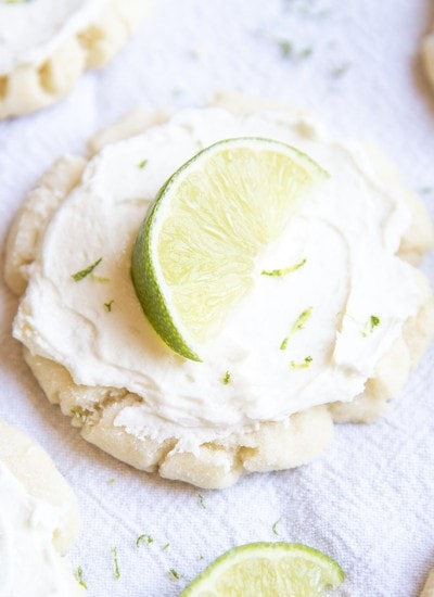 A sugar cookie topped with white frosting, lime zest, and a lime wedge.