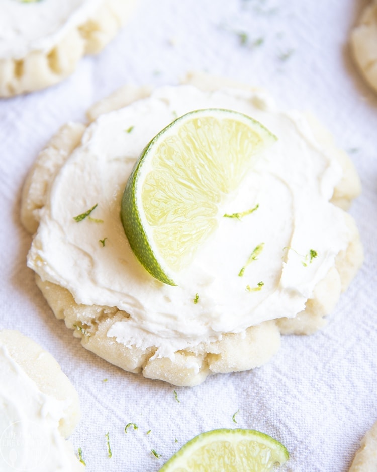 A sugar cookie topped with white frosting, lime zest, and a lime wedge.