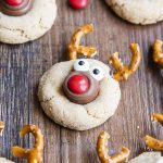 Peanut butter cookies decorated to look like a reindeer with pretzel antlers, candy eyes, and an m&m nose.