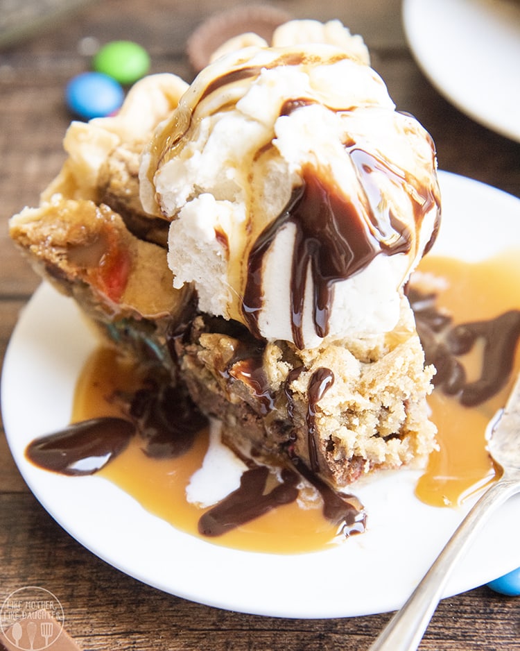 A slice of candy bar pie topped with vanilla ice cream and chocolate syrup. 