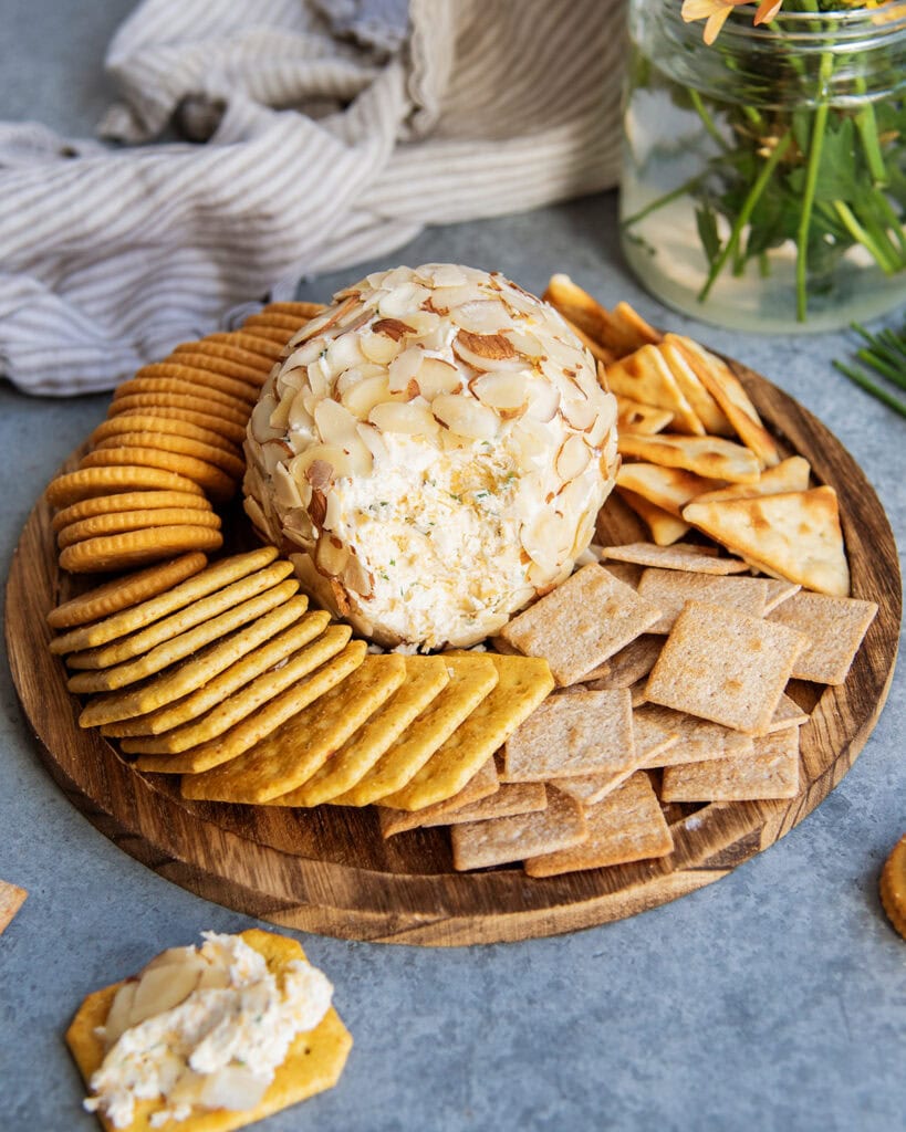 A classic cheese ball with the outside opened up to show the center of it, surrounded by crackers.