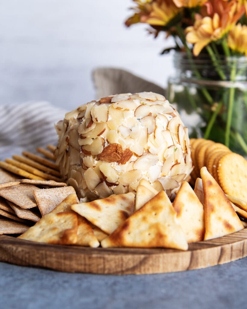A cheese ball covered in sliced almonds, on a wooden board with crackers.