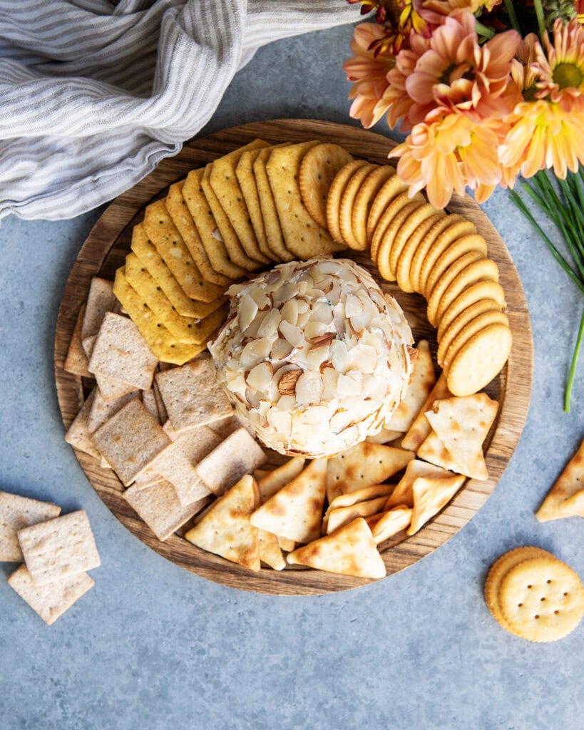 An above view of a classic cheese ball on a wooden board with crackers.