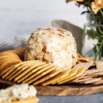A classic cheese ball with the outside opened up to show the center of it, surrounded by crackers.