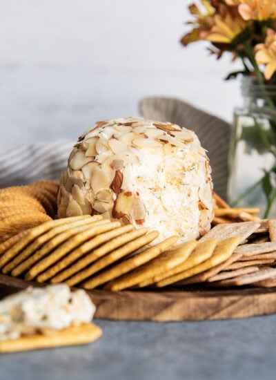 A classic cheese ball with the outside opened up to show the center of it, surrounded by crackers.