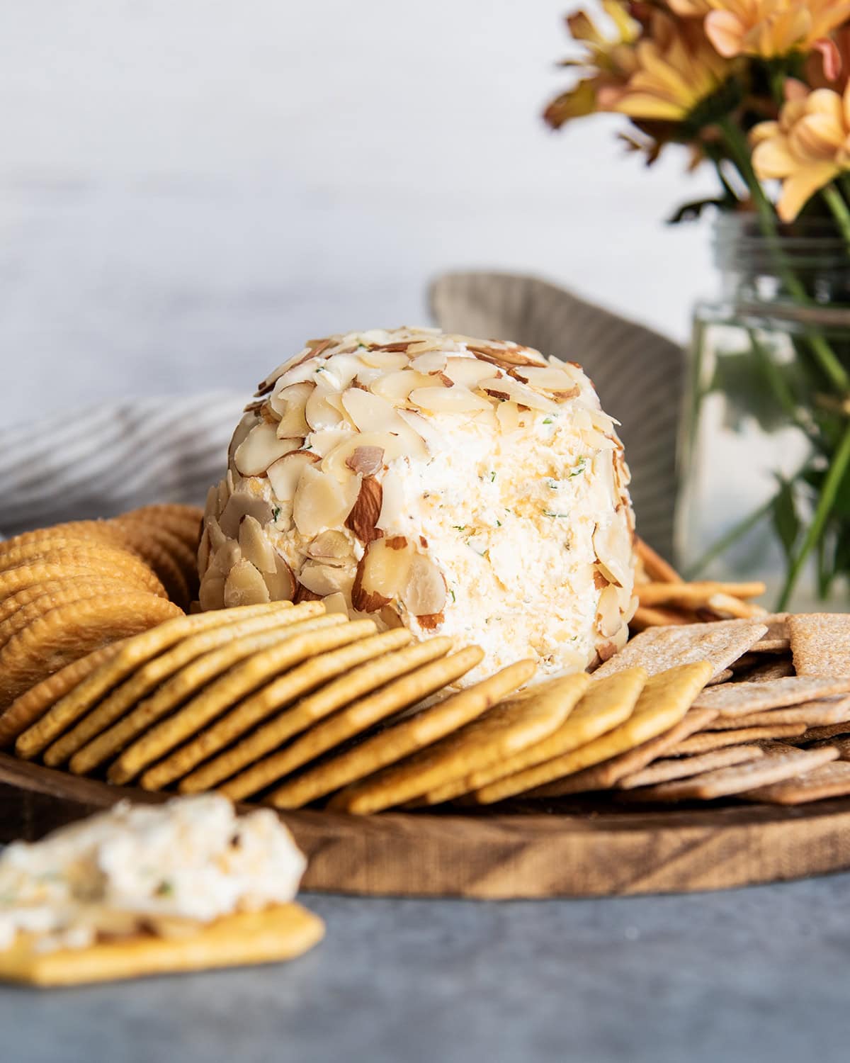 A classic cheese ball with the outside opened up to show the center of it, surrounded by crackers.