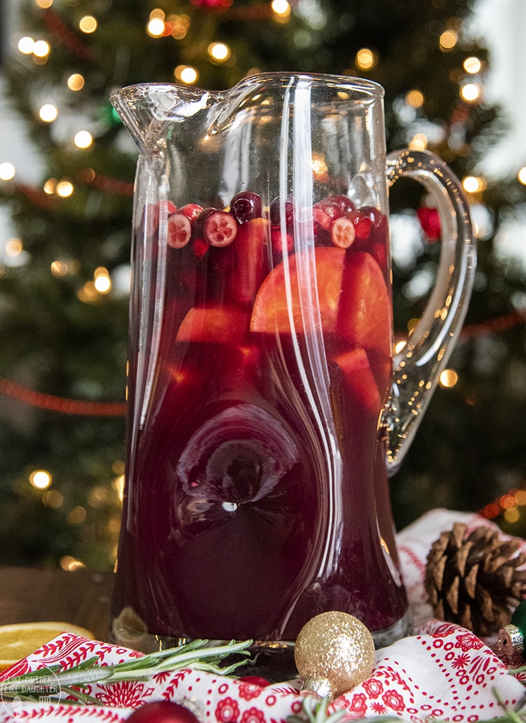 A pitcher full of a dark red Christmas drink, with cranberries, and orange pieces. 