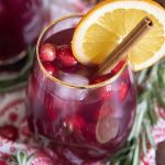 A glass of alcohol free Christmas sangria with cranberries and a cinnamon stick in it.