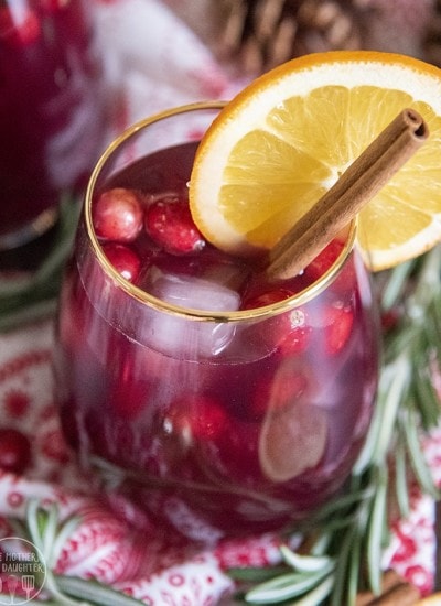 A glass of alcohol free Christmas sangria with cranberries and a cinnamon stick in it.
