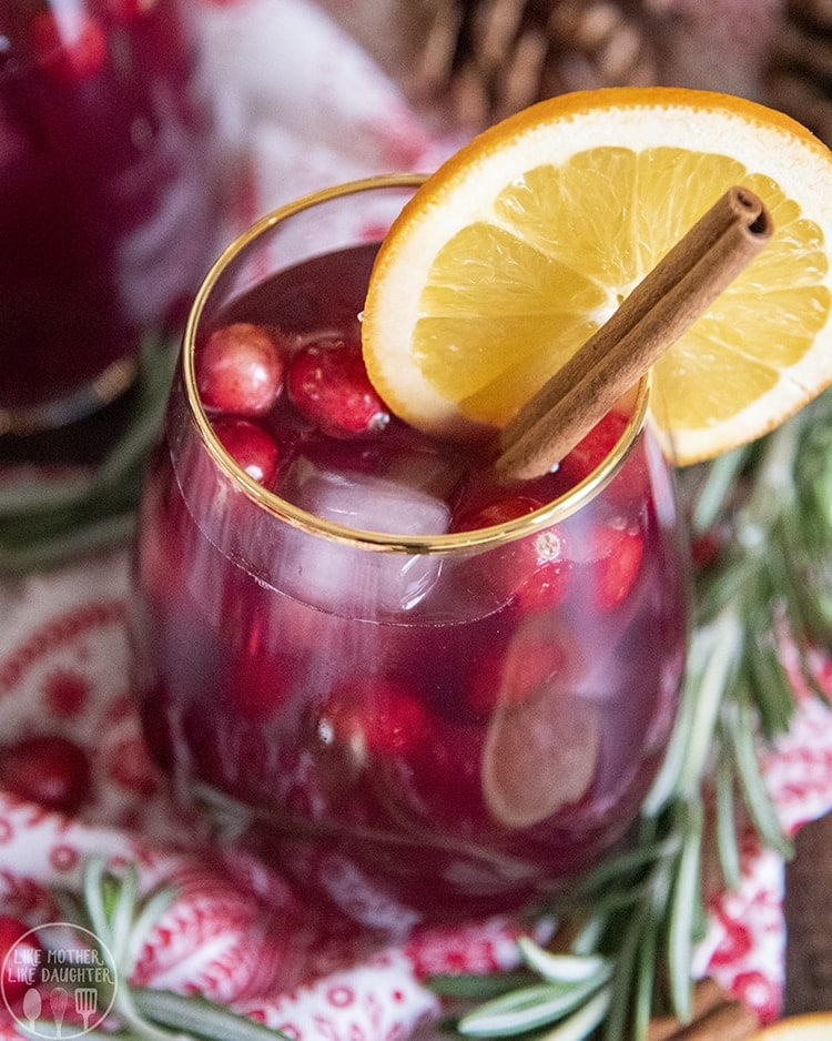 A glass of alcohol free Christmas sangria with cranberries and a cinnamon stick in it.