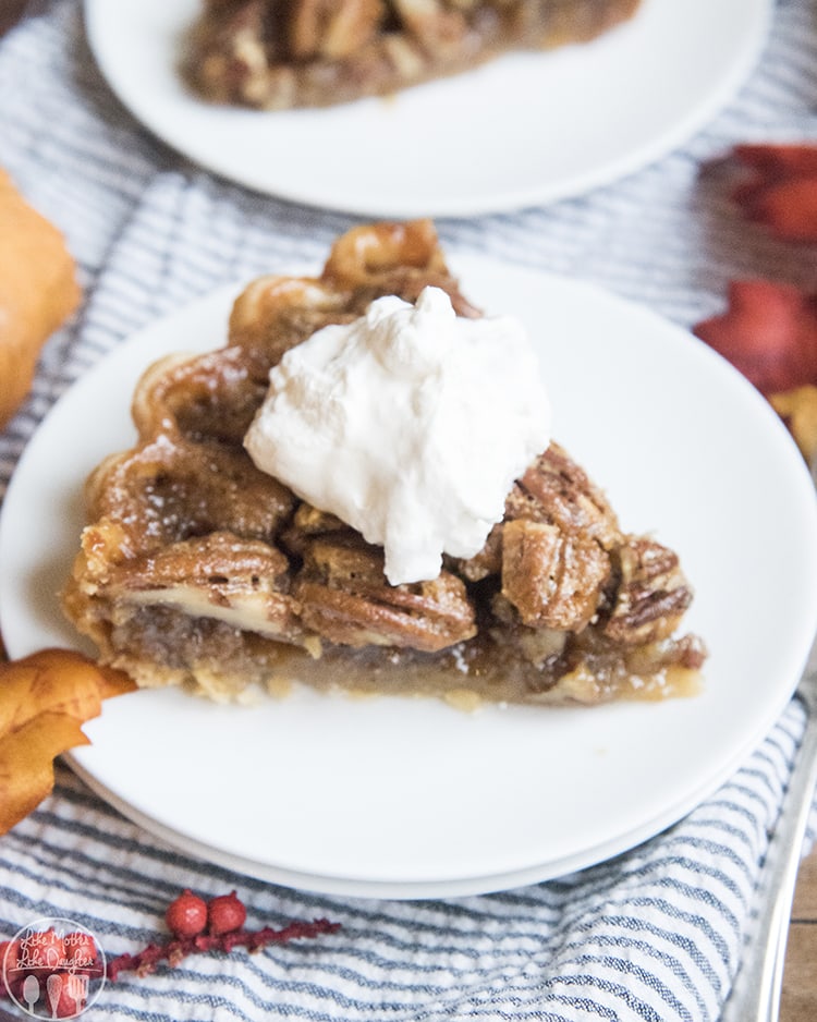 A piece of pecan pie topped with fresh whipped cream on a plate.