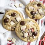 Three peppermint bark chocolate chip cookies topped with chocolate chips, peppermint bark pieces, and candy cane pieces.