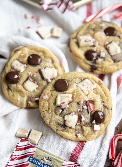 Three peppermint bark chocolate chip cookies topped with chocolate chips, peppermint bark pieces, and candy cane pieces.