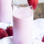 Close up image of strawberry yogurt smoothie in a glass with a strawberry on the glass rim.