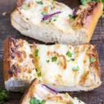 Slices of chicken alfredo french bread pizza on a wood backdrop with cheese and parsley on top.