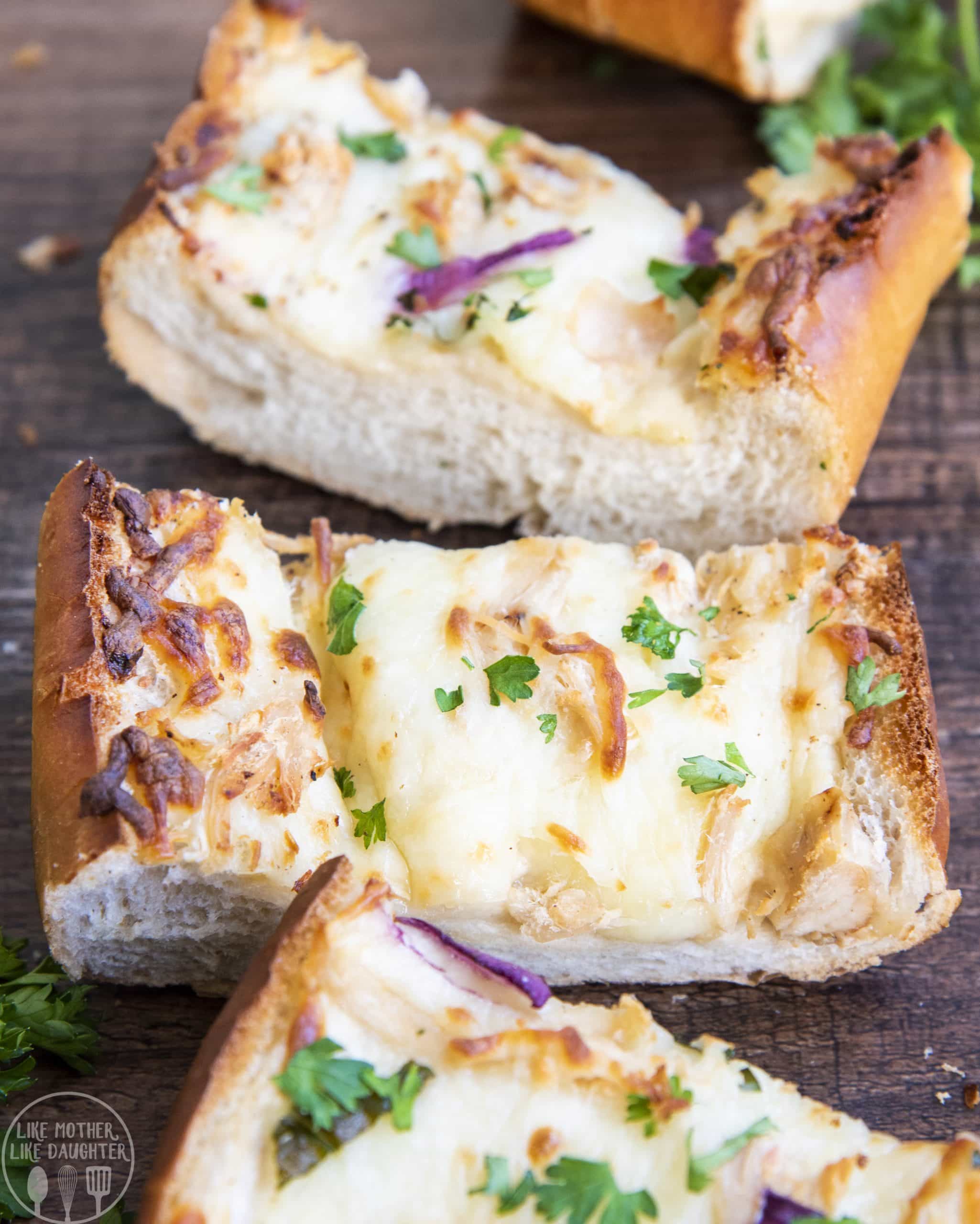Slices of chicken alfredo french bread pizza on a wood backdrop with cheese and parsley on top.