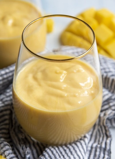 Above image of a glass of mango smoothie with mango in the background.